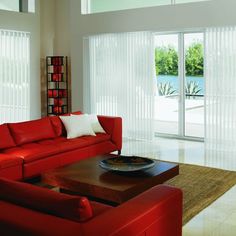 a living room with red couches and white blinds on the sliding glass doors that lead to an outdoor pool