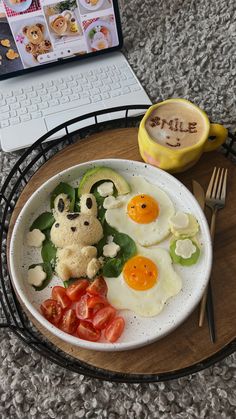 a plate with eggs, tomatoes and cucumbers on it next to a laptop