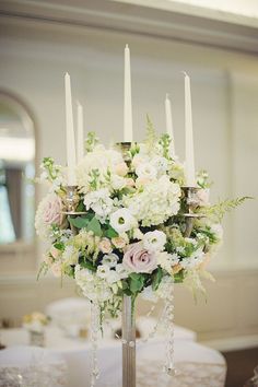 a tall vase filled with white and pink flowers on top of a table covered in candles