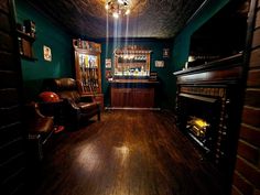 a room with wood floors and green walls has a bar in the corner, two leather chairs on either side