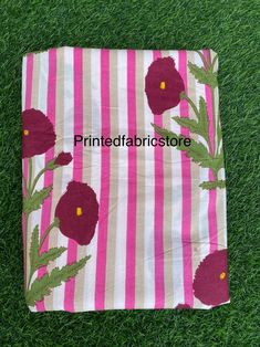 a pink and white striped towel with flowers on it sitting in the grass next to some green grass