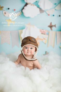 a baby wearing a pilot's hat and sitting in the clouds with his name on it