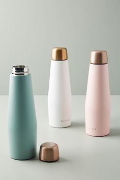 three different colored bottles sitting next to each other on a white counter top, one with a gold lid