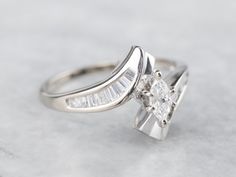 The polished lines on this marquise cut diamond engagement ring is a thing of spectacular beauty! The sleek curves of the center gem echo in the elegant design of the bypass style mounting, which is encrusted in sparkling baguette-cut diamonds. Metal: 14K White Gold Gem: Diamond .16 Carats, VVS in Clarity, E in Color Gem Measurements: 3.0 x 5.3 mm, Marquise Cut Accents: 20 Diamonds totaling .50 Carats, VVS in Clarity, G in Color Ring Size: 7.75 Marks: "14K..." Stamped on the inside band Marquise Cut Diamond Ring With Baguette Diamonds, Marquise Cut Diamond Engagement Rings, Inspiration Pics, Marquise Diamond Engagement Ring, Marquise Ring, Bypass Ring, Engagement Ring White Gold, Marquise Cut Diamond, White Gold Diamond Rings