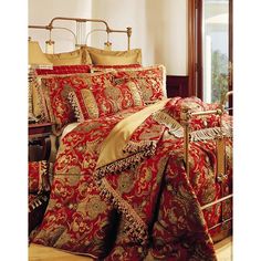 a bed with red and gold comforters on top of it in a room next to a window