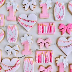 pink and white decorated cookies are arranged on a marble countertop with candles, bows, hearts, and other decorations