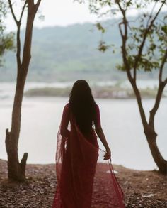 a woman in a red sari walking down a path next to trees and water