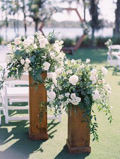 two wooden vases filled with white flowers on top of a grass covered field next to chairs