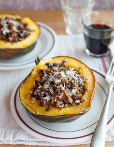 two stuffed squash halves with meat and cheese on the top, sitting on a plate next to a glass of red wine