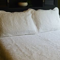 a white bed with two pillows on top of it and a potted plant in the corner