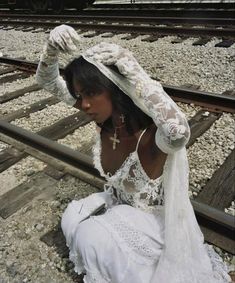 a woman sitting on train tracks with her hair in the air and wearing a white dress