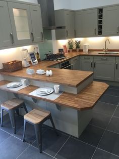 a kitchen with grey cabinets and wooden counter tops, two stools in front of the island