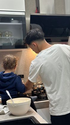 a man standing over a child in a kitchen preparing food on top of a stove