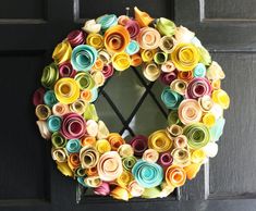 a wreath made out of rolled up paper flowers hangs on the front door's black door