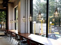 a long table with lots of chairs in front of large windows and lights hanging from the ceiling