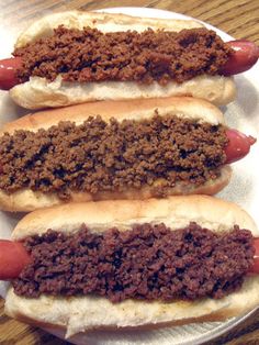 three hot dogs on buns covered in chili and ground beef sitting on a paper plate