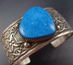 "VINTAGE NAVAJO BRACELET DESCRIPTION: This cuff features a gorgeous specimen of high blue turquoise on a cuff with intricate stamp work. The gemstone is secure in smooth bezel, on a foundation of heavy gauge vintage sterling silver. This bracelet will be a cherished addition to your collection of fine vintage Native American jewelry. MEASUREMENTS: Interior of the cuff measures 5 3/4\" with an additional 1 1/4\" slightly adjustable gap. Total circumference: 7\" Measures 2 1/2\" straight across th Southwestern Blue Cuff Bracelet As Gift, Adjustable Blue Engraved Cuff Bracelet, Blue Cuff Bracelet With Patina As A Gift, Blue Patina Cuff Bracelet As Gift, Blue Cuff Bracelet With Patina For Gifts, Blue Patina Cuff Bracelet As A Gift, Bohemian Blue Stamped Bracelets, Unique Blue Cuff Bracelets, Bohemian Stamped Blue Bracelets