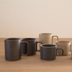 several coffee mugs lined up on a wooden table with white wall in the background