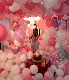 a woman standing in front of a cake surrounded by pink and white balloons on the ceiling