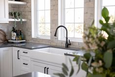 a kitchen with white cabinets and black counter tops next to a window filled with greenery