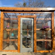 a small wooden structure with glass doors and flowers on the outside, in front of a blue sky