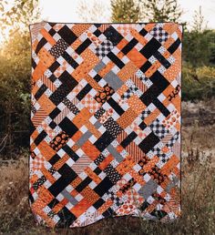 an orange and black quilt hanging in the grass