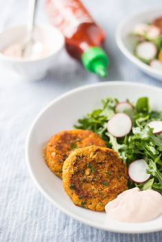 two crab cakes on a white plate with greens and sauces next to the dish