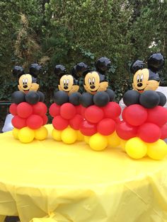 mickey mouse balloons sitting on top of a yellow table with trees in the back ground