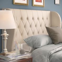 a white headboard in a bedroom next to a lamp and pictures on the wall