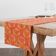 an orange table runner with pumpkins on it and two wine glasses sitting on top