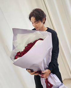 a young man holding a bouquet of roses in his hand and looking down at it