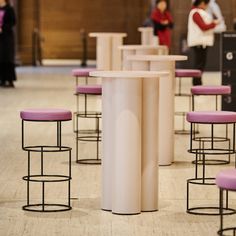 several stools and tables in a room with people standing around the area behind them