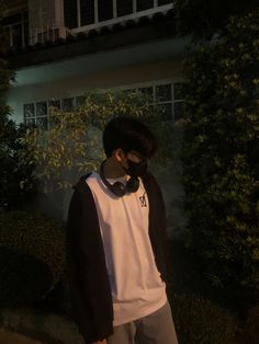 a man wearing a black and white shirt standing in front of a house at night