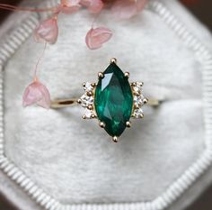 an emerald colored ring sitting on top of a white cloth with pink flowers in the background