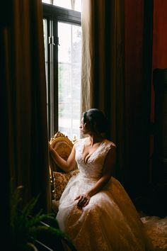 a woman in a wedding dress sitting on a chair looking out the window at something outside