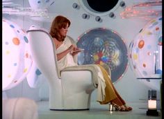 a woman sitting in a white chair looking at her cell phone while wearing high heels