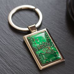 a green circuit board keychain sitting on top of a black table next to a cell phone