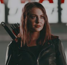 a woman with scissors in her hand and wearing a black leather jacket is looking at the camera