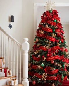 a decorated christmas tree with red and green ribbons on it in front of a staircase