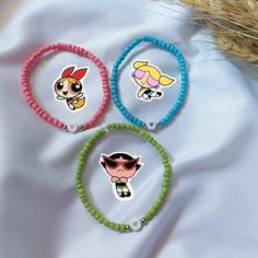 three bracelets with cartoon stickers on them sitting on a white sheet next to some wheat