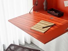 a red desk with a pen and paper on it in front of a white curtain