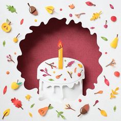 a birthday cake with a lit candle surrounded by fall leaves