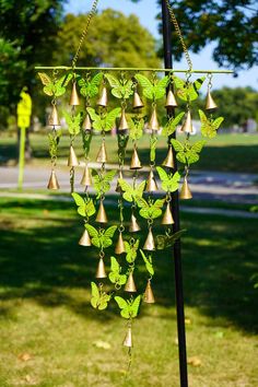 a wind chime with green leaves and bells hanging from it's side on a pole