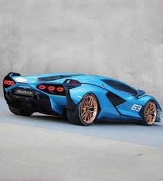 a blue sports car parked in front of a cement wall with orange rims on it