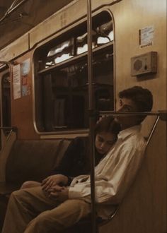 two people sitting on a subway car looking at their cell phones while the train is stopped