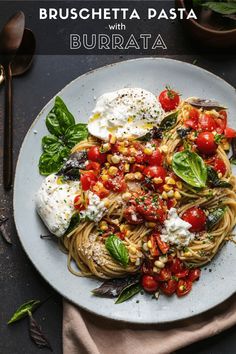 a plate of pasta with tomatoes, corn and spinach on it next to two spoons