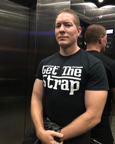 a man is standing in an elevator with his hand on his hip and wearing a t - shirt that says get the strap