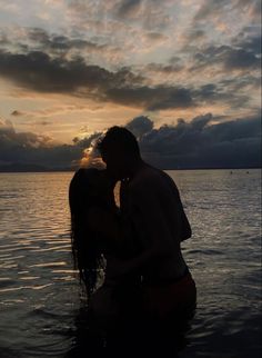 a man and woman kissing in the water under a cloudy sky at sunset or dawn