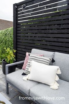 a grey couch sitting on top of a patio next to a black fence and potted plants