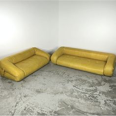 two yellow couches sitting next to each other in a room with cement flooring